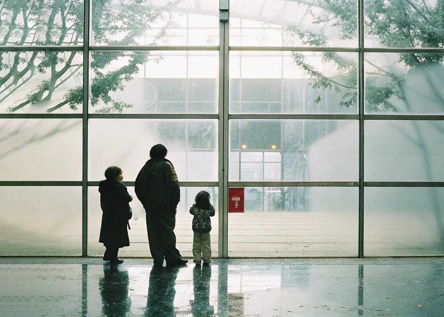 Unos niños mirando a través de un ventanal gigante de una institución gigante